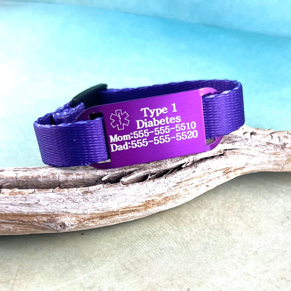 Purple kids medical alert bracelet displayed on a piece of wood.