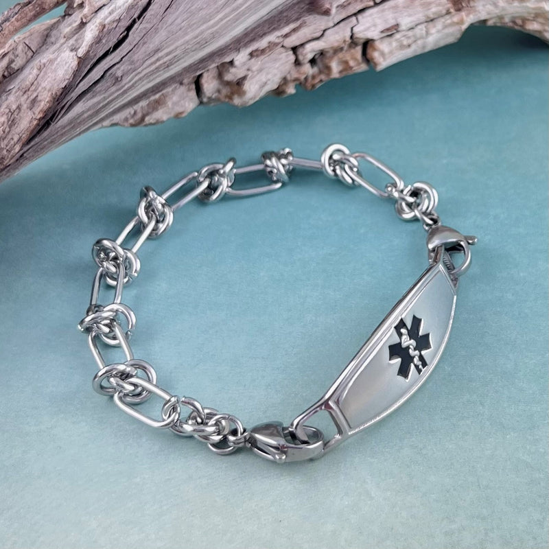 Barbed wire stainless steel medical alert bracelet displayed in front of a piece of wood.
