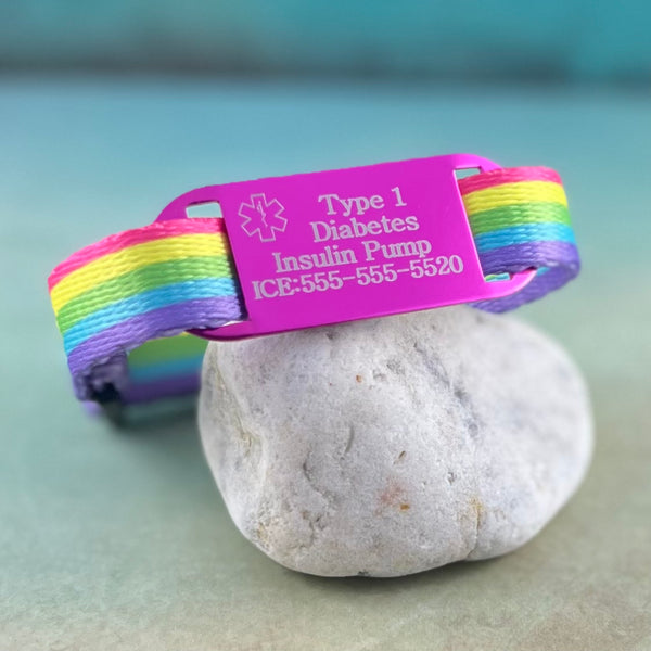 Rainbow print kids medical alert bracelet  with pink type 1 diabetes medical ID tag displayed on a rock.