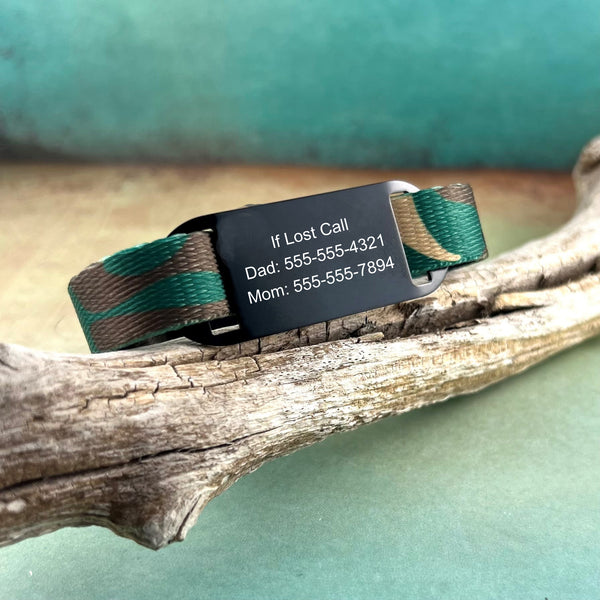 Camouflage print kids identification bracelet with personalized black ID tag displayed on a piece of wood.