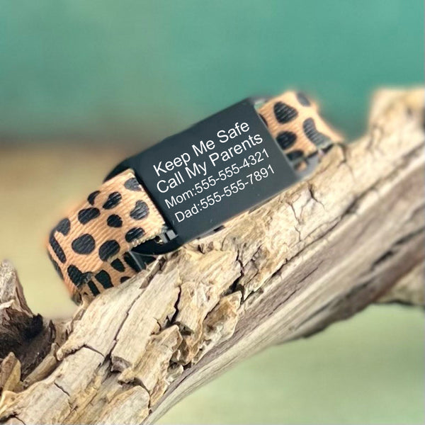 Cheetah print nylon identification bracelet with black custom engraved ID tag displayed on a piece of wood.