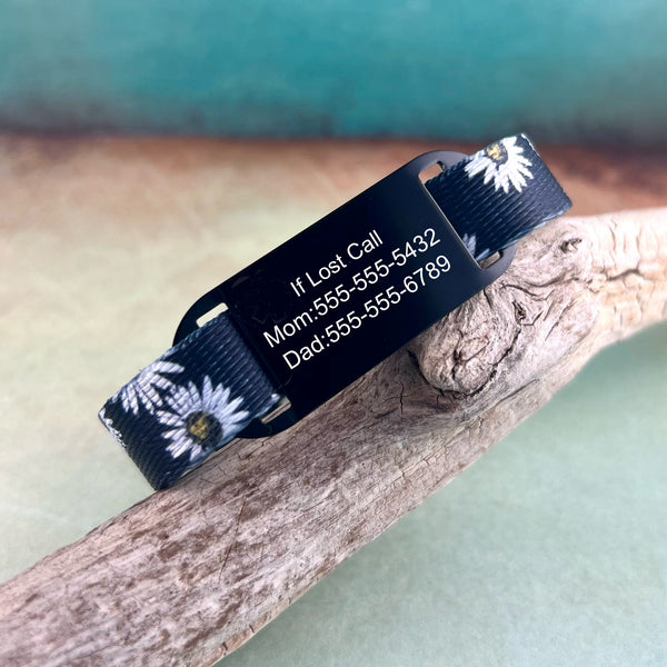 Black daisy print kids ID bracelet with a personalized black ID tag displayed on a piece of wood.