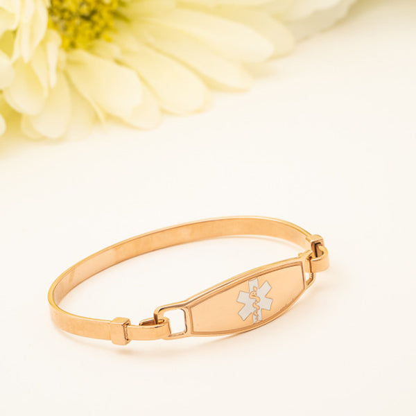 Rose Gold plated bangle medical alert bracelet with white star of life symbol with white flower background.