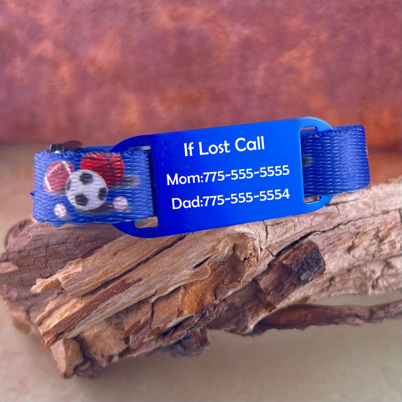 Blue nylon medical bracelet printed with soccer balls, footballs, basket balls with a blue ID tag displayed on a piece of wood.