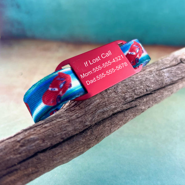 Red and blue race car ID bracelet for kids with red personalized ID tag displayed on a piece of wood