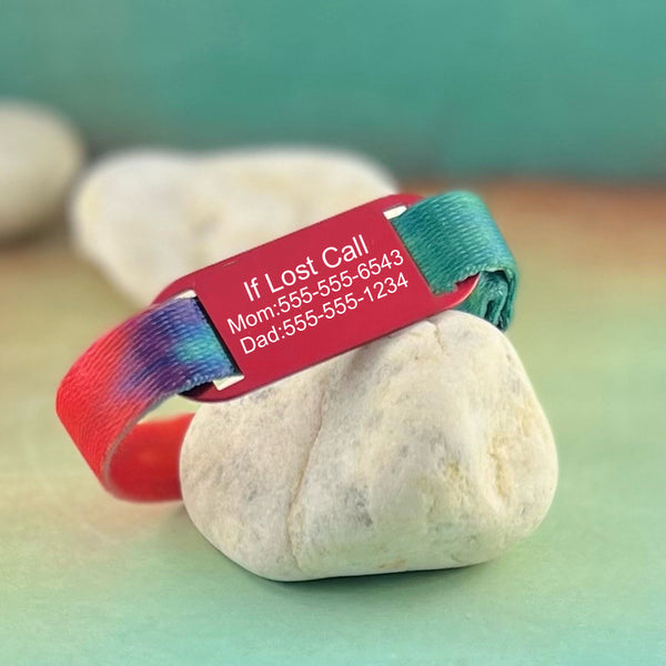 Tie Dye print kids ID bracelet with personalized red ID tag displayed on a rock.