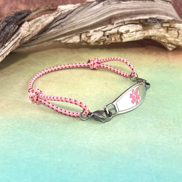 Adjustable pink stretch cord medical alert bracelet with pink star of life stainless steel medical ID tag displayed in front of a piece of wood.