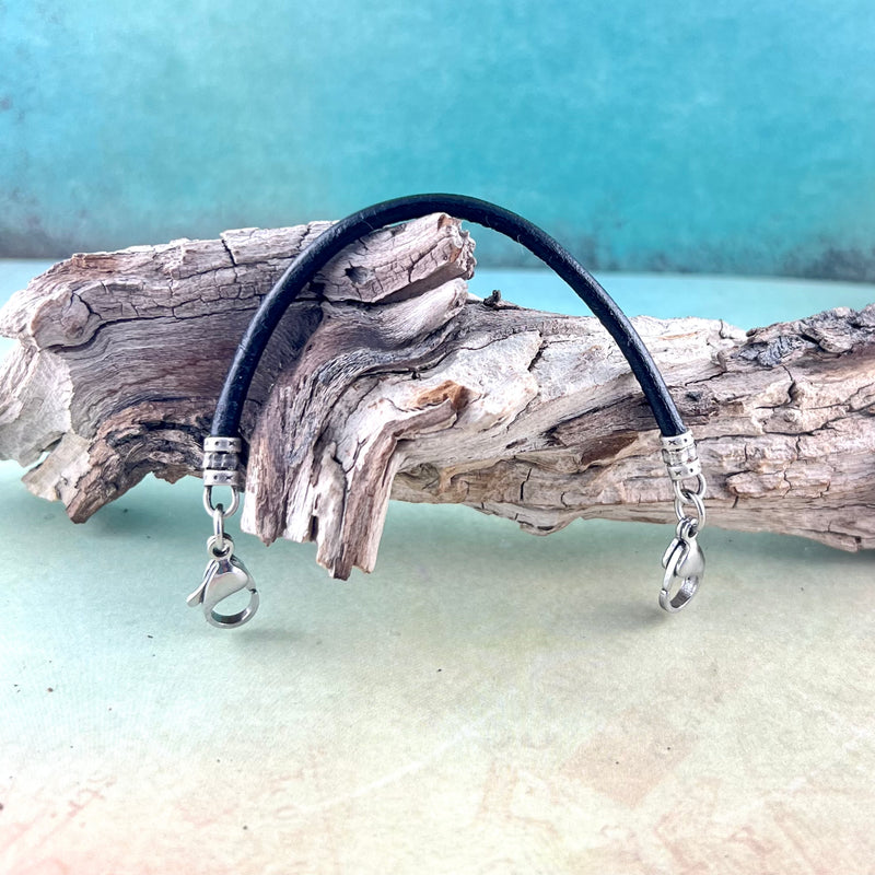 Black leather replacement medical alert bracelet with  stainless steel lobster clasps displayed on a piece of wood.