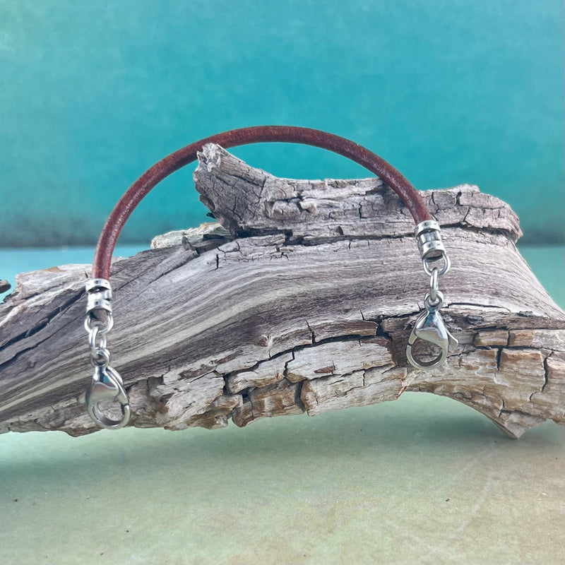 Replacement medical alert bracelet in brown leather with stainless steel lobster clasps hanging on a piece of wood.