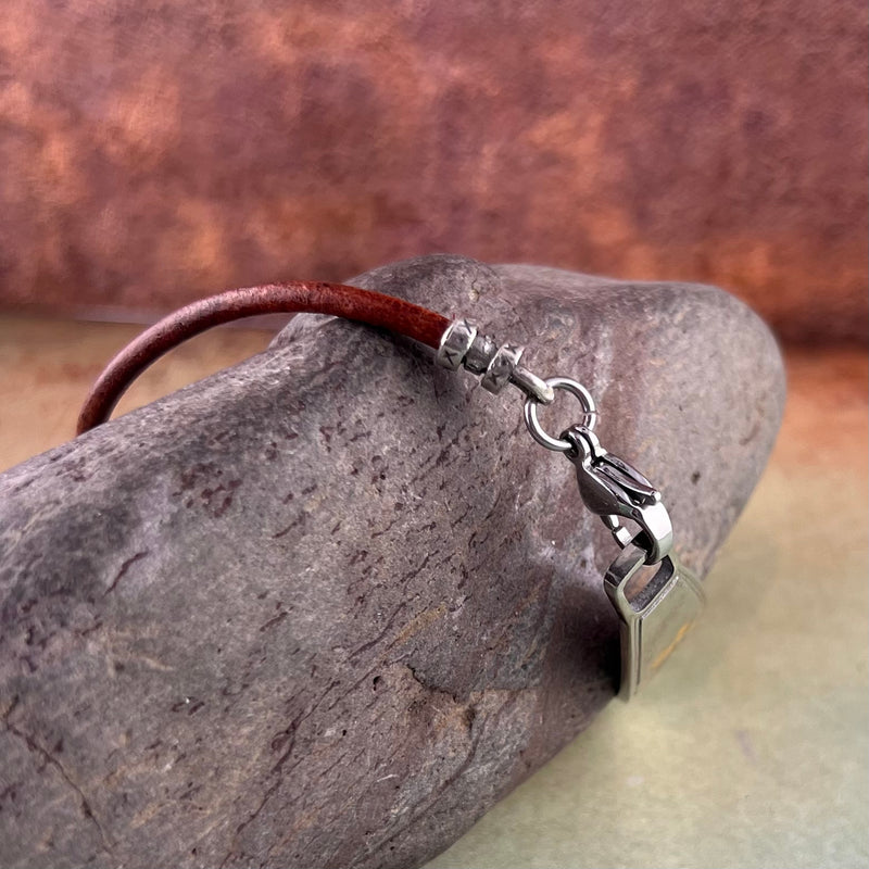 Brown leather medical alert bracelet displayed on a rock.