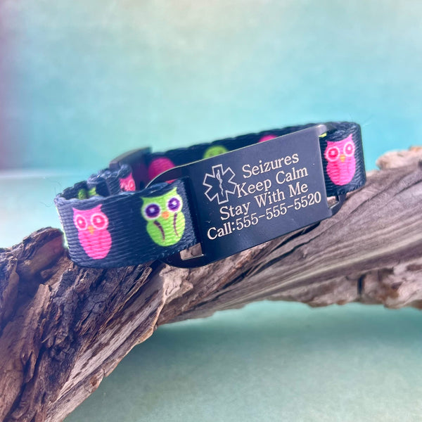 Green and pink owl print kids medical alert bracelet displayed on a piece of wood.