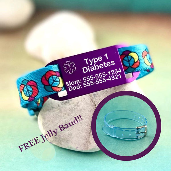 Blue medical alert bracelet with flower design peace signs displayed on a rock with a blue jelly band.