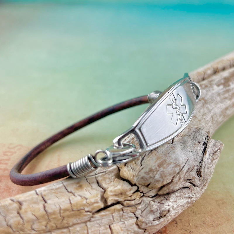 Brown leather medical alert bracelet displayed on a piece of wood.