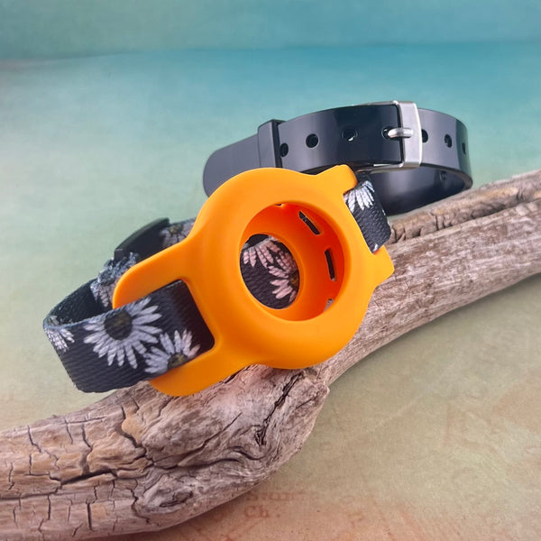 Kids AirTag bracelet in black and white daisy print with orange AirTag holder and black silicone bracelet displayed on a piece of wood.