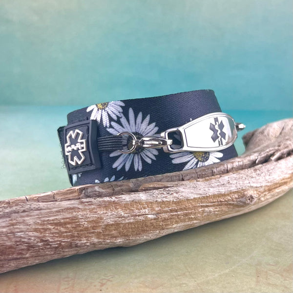 Adjustable medical alert bracelet for women in black nylon with a daisy print. displayed on a piece of wood.