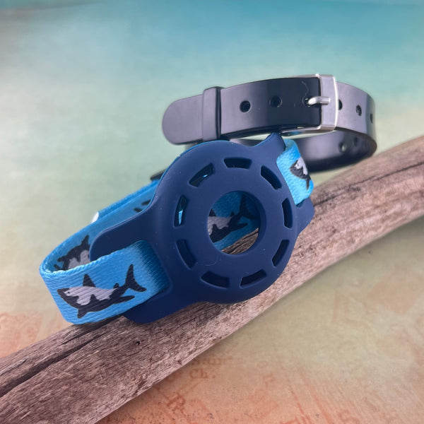 Blue Airtag bracelet with shark print with blacksilicone band displayed on a piece of wood.