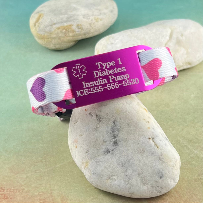 Purple and pink heart print kids medical alert bracelet with pink medical ID tag which is engraved with a sample engraving.