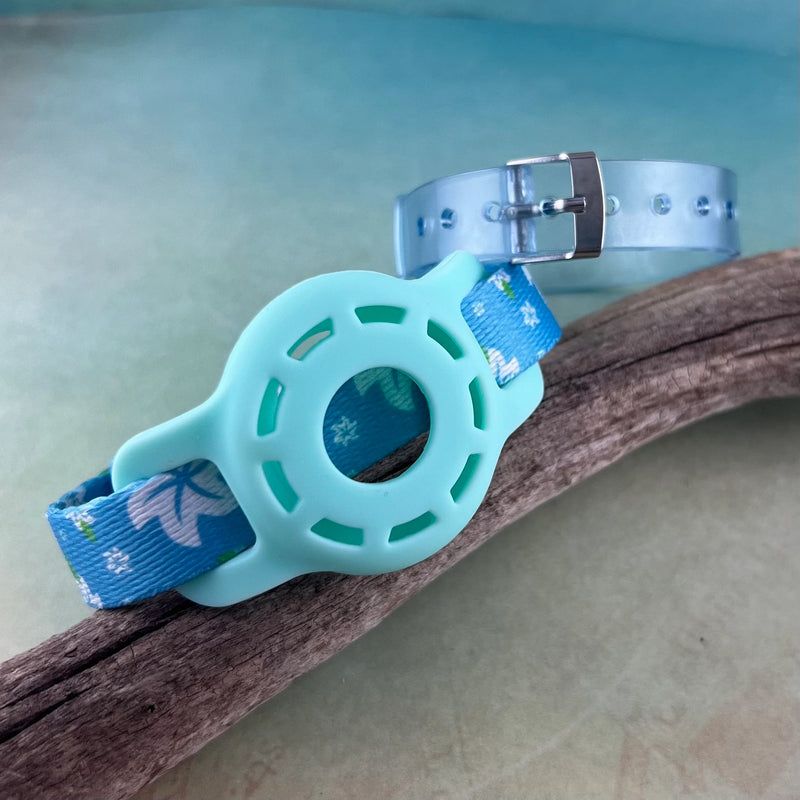 Kids Airtag bracelet in a light blue Hawaiian print with blue AirTag holder and blue jelly band displayed on a piece of wood.