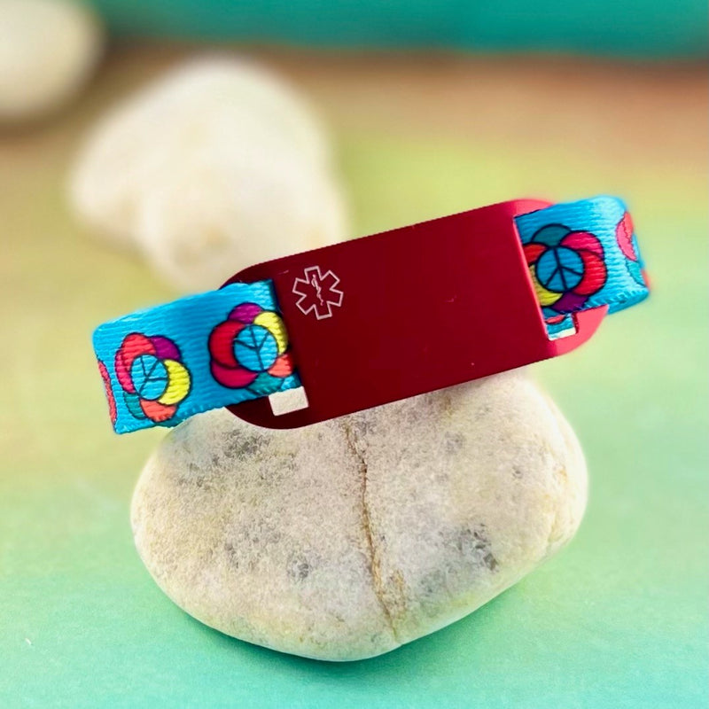 Blue peace sign and flower design medical alert bracelet with red medical ID tag displayed on a rock.