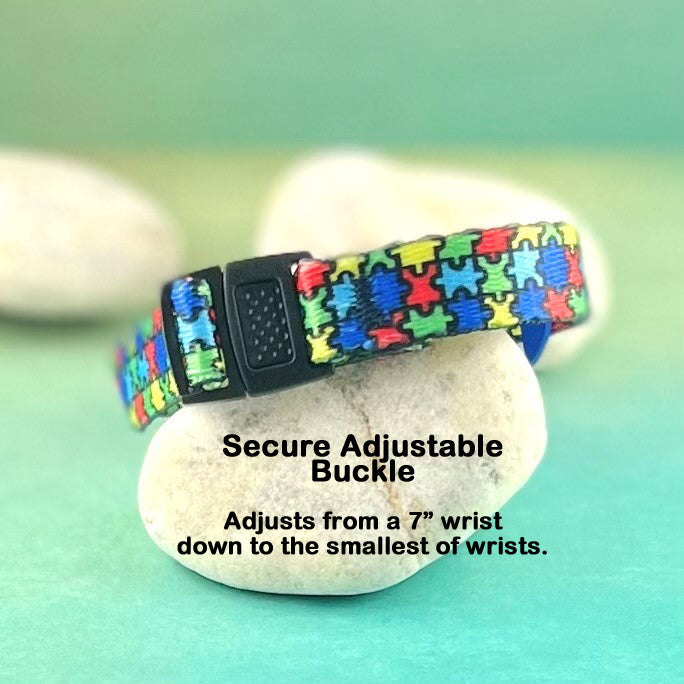 Center push black adjustable buckle on a puzzle replacement medical alert bracelet displayed on a rock.