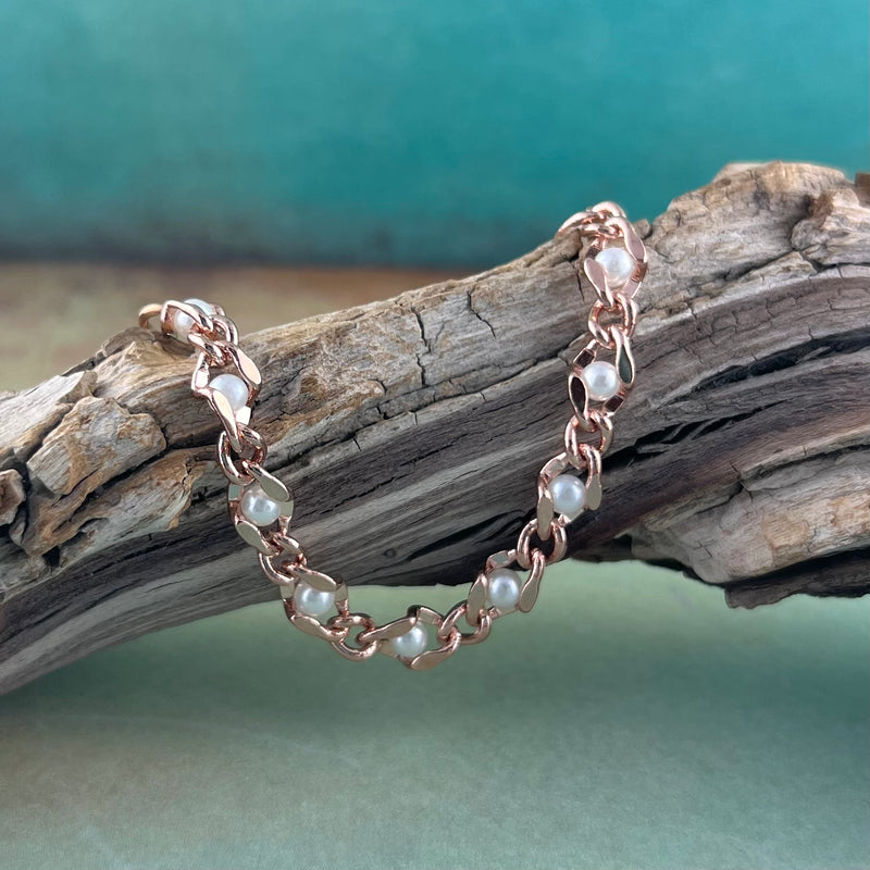 Rose gold and pearl bracelet displayed on a piece of wood.