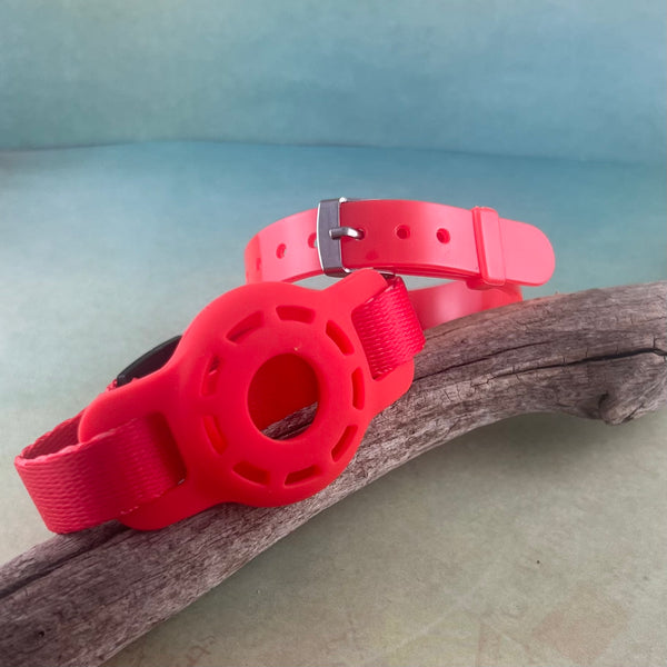 Red kids AirTag wristband and silicone band displayed on a piece of wood.