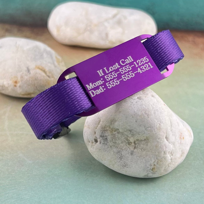Purple kids ID bracelet with engraved purple identification tag displayed on a rock.