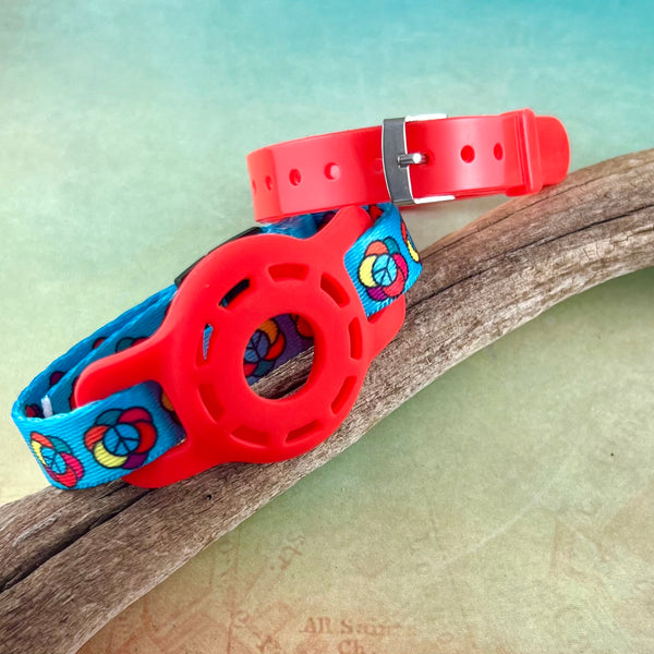 Kids Airtag bracelet in light blue with printed peace signs with red AirTag holder and red jelly band displayed on a piece of wood.