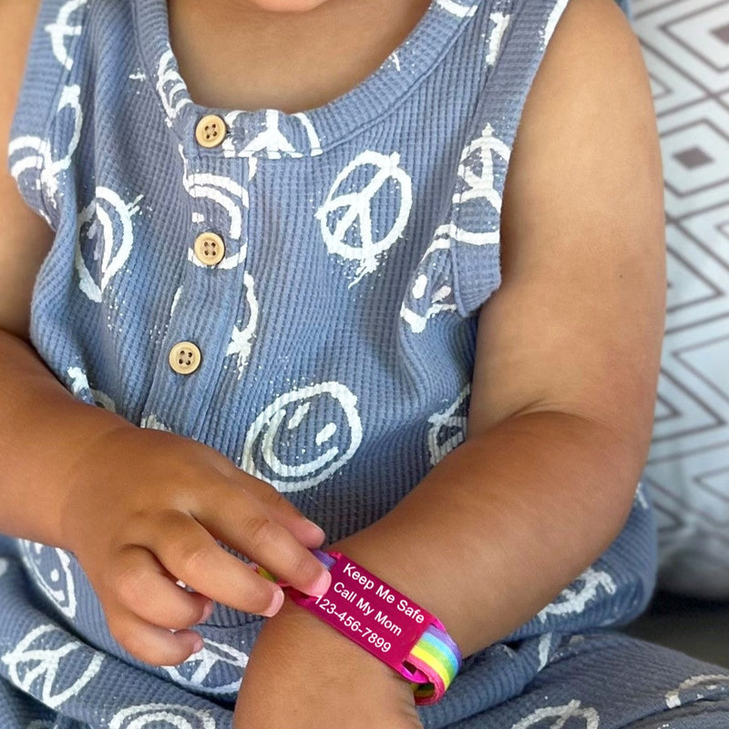 Child wearing rainbow print identification bracelet with engraved pink ID tag.