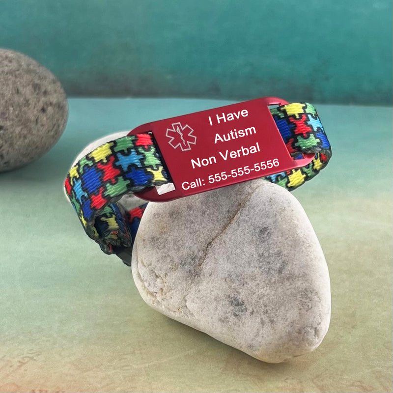 Puzzle print medical alert bracelet with personalized medical ID tag displayed on a rock.