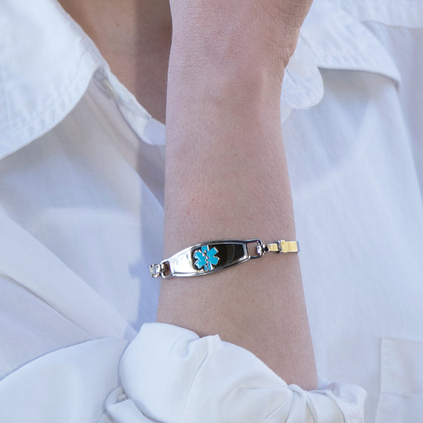 Stainless steel bangle medical alert bracelet with turquoise star of life medical tag on woman's wrist wearing a white shirt.