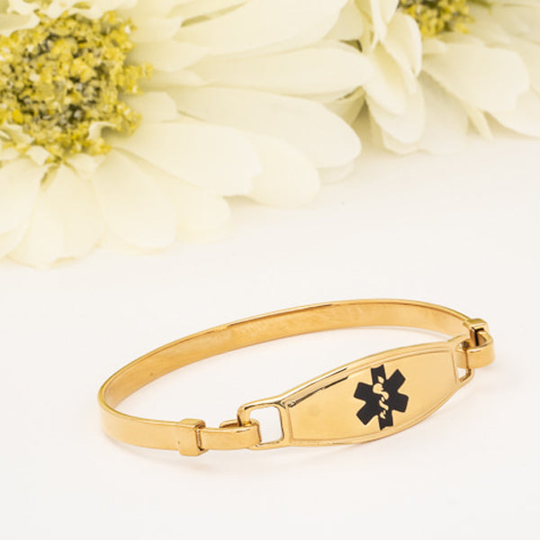 Gold plated bangle medical alert bracelet with black star of life symbol and white flowers in the background.