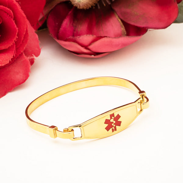 Gold plated bangle medical alert bracelet with red star of life symbol and red flowers in the background.