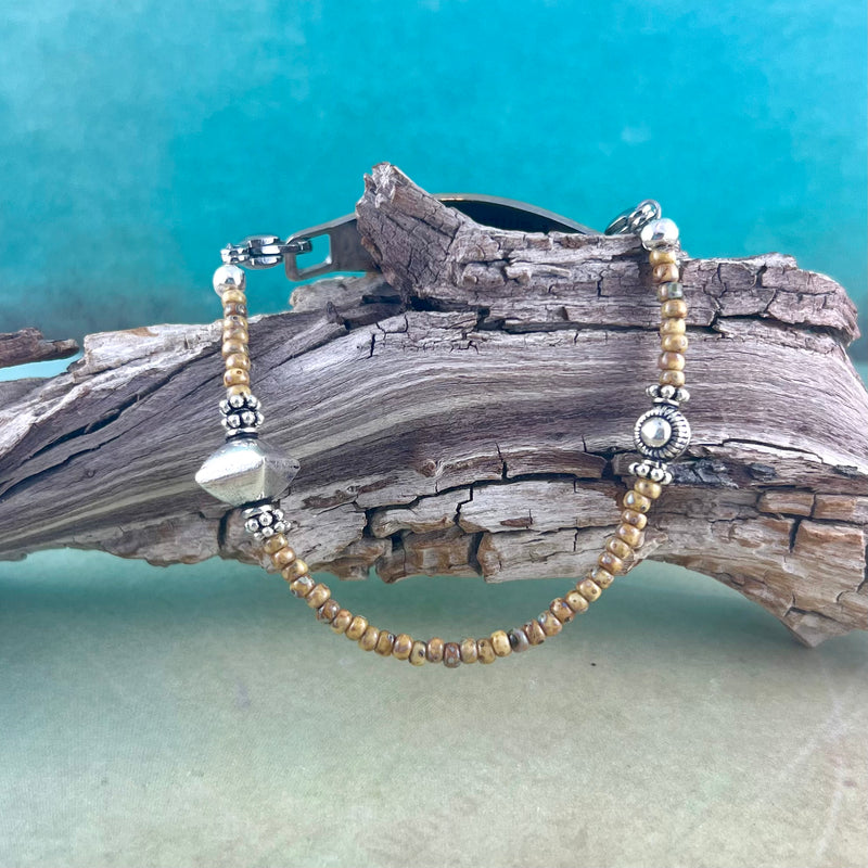 Sand colored and silver beaded bracelet displayed on a piece of wood.