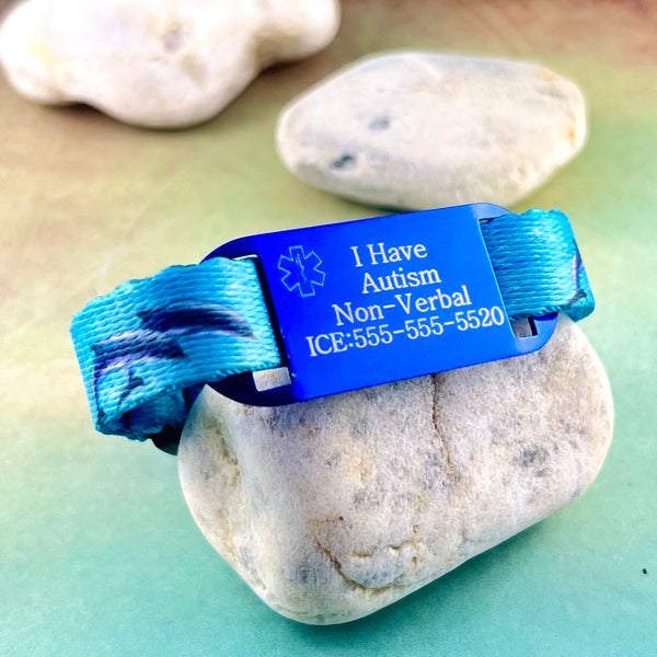 Dolphin print nylon blue medical alert bracelet with a personalized medical ID tag displayed on a rock.