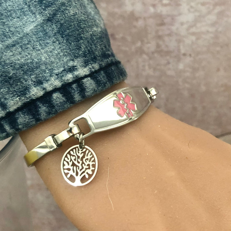 Wrist with stainless steel bangle medical alert bracelet and pink star of life medical tag with tree of life charm.