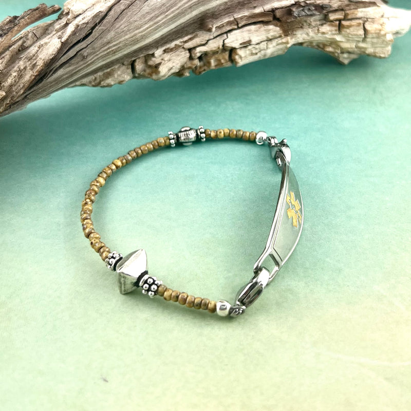 Sand colored and silver beaded medical alert bracelet displayed in front of driftwood.