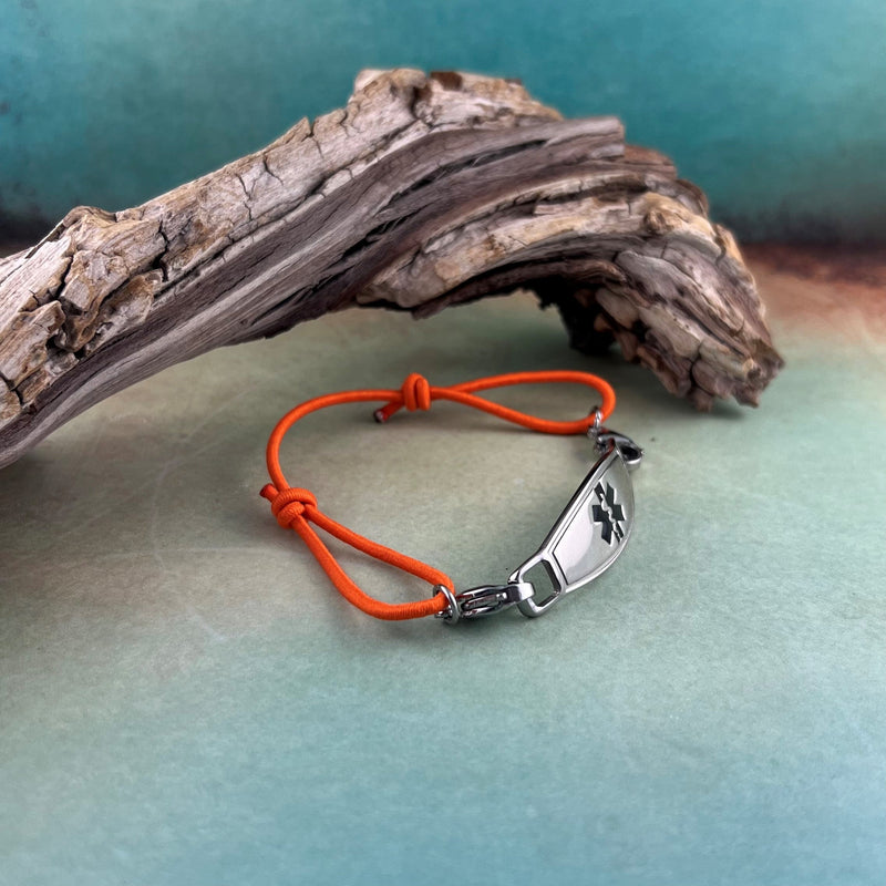 Orange adjustable stretch medical alert bracelet displayed in front of a piece of wood.
