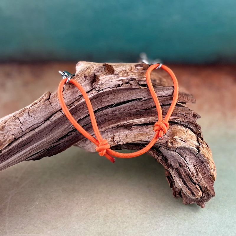 Orange adjustable stretch bracelet displayed on a piece of wood.